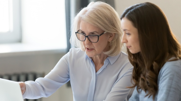 Two women look at laptop screen.